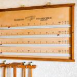 Wall-mounted billiard measuring device with four scales and a cue rack.