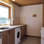 Kitchen with washing machine, sink, and window. Wooden surface and tiled floor.