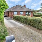 Drive to a house with red brick and green hedge fence.