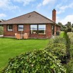Red brick house with garden and seating. View of water and sky.