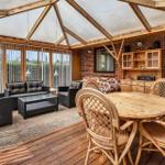 Terrace with seating area, dining table, and wooden deck. Glass roof and wooden frame visible.