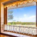 Kitchen window with sea and green view, white lace curtain and wooden frame.