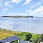House with view of island and sea under blue sky with white clouds.