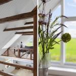 Dachgeschoss mit Holzbalken und Aussicht auf grünes Feld. Blumen in Glasvase vor Fenster.