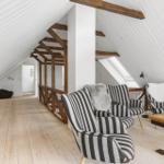 Dachgeschoss mit Holzbalken, Streifen-Sofa und Holztisch.