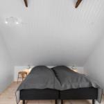 Schlafzimmer mit Doppelbett, Holzboden und schrägen weißen Wänden. Wandbilder und Nachttische sind vorhanden.
