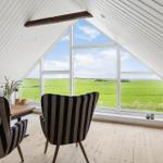 Zimmer mit schrägen Wänden, großem Fenster und Blick auf grünes Feld.