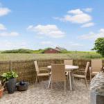 Terrasse mit Tisch und Stühlen, Blick auf Feld und rote Scheune unter blauem Himmel.
