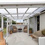 Terrasse mit Glasdach, zwei Stühlen und Pflanzen. Durchgang ins Haus.