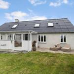 Ein Haus mit grauer Fassade, Dachgauben und einer Terrasse mit Gartenmöbeln.