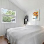 Schlafzimmer mit weißer Holzwand, Bett, Fenster und Wandbild.