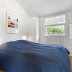Schlafzimmer mit blauer Bettdecke, Fenster und Spiegel an der Wand.