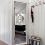 Badezimmer mit runder Spiegel, schwarzer Waschbeckenkonsole und Toilette. Regenmantel hängt an Wandhalter.