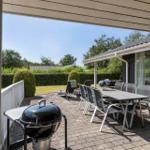 Terrasse mit Grill, Tisch und Stühlen. Hintergrund: Garten mit Hecke und Bäumen.