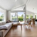 Wohn- und Essbereich mit Sofa, Stuhl und Tisch. Große Fenster und Tür zu Garten.