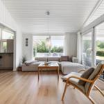 Wohnraum mit Sofa, Sessel und Holzboden. Durchgang zur Küche und Terrasse.