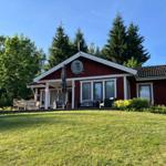 Rotes Holzhaus mit Terrasse, Garten und Bäumen im Hintergrund.