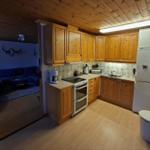 Küche mit Holzmöbeln, Kühlschrank und Blick in Wohnzimmer mit Sofa.