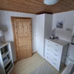 Schlafzimmer mit Holzboden, weißen Schränken und Holztür. Decke aus Holz, Wandbilder und Lampe.
