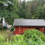 Rotes Holzhaus am See mit Boot und Holzsteg. Umgeben von Wald und Grünflächen.