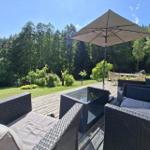 Terrasse mit Sitzgruppe, Sonnenschirm und Blick auf grünen Garten und Wald.