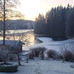 Frosted lake with forest and small cabin at sunrise.