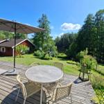 Terrasse mit Tisch, Stühlen und Sonnenschirm. Blick auf Garten, Wald und Haus.