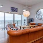 Wohnzimmer mit braunem Ledersofa, runden Fenster und Blick aufs Meer.