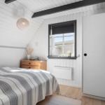 Schlafzimmer mit Bett, Nachttisch und Fenster. Weiße Wände, Holzboden und Deckenbalken.