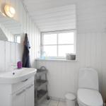 Badezimmer mit Waschbecken, Toilette und Fenster. Weiße Holzwandverkleidung und Spiegel.