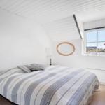 Schlafzimmer mit Bett, Fenster und Holzboden. Decke weiß, Wand mit Spiegel.