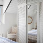 Schlafzimmer mit Fenster, Stuhl und Kleiderschrank mit Spiegeltür.