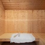 Holzsauna mit Sitzbank, weißer Decke und Bürsten.