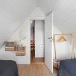 Zimmer mit zwei Betten, weißen Wänden und Holzboden. Tür führt in einen Flur.