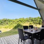 Terrasse mit Tisch und Stühlen, Blick auf grüne Landschaft unter blauem Himmel.