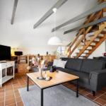 Wohnzimmer mit Sofa, Couchtisch und Holztreppe. Terrakottaboden und weiße Wände.