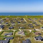 Aerial view of coastal holiday homes with green dunes and blue sea in the background.