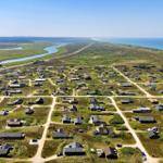 Aerielansicht von Häusern entlang einer Küstenstraße mit Fluss und Meer im Hintergrund.