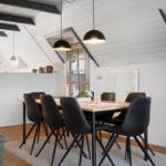 Esszimmer mit Holztisch, schwarzen Stühlen und schwarzem Deckenlicht. Weiße Wände und Holzbalken.