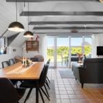 Wohn- und Essbereich mit Holztisch, Sofa und Terrassentür. Deckenbalken und Terrasse sind sichtbar.