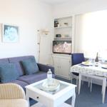 Wohnzimmer mit Sofa, Esstisch und Fernseher. Fenster mit Vorhängen. Tisch mit Tischdecke und Flasche.