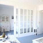 Essbereich mit Tisch, Flasche und Gläsern. Durchgehendes Fenster mit Glaspartien. Hintergrund: Schrank und Tür.