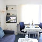 Wohnzimmer mit Sofa, Esstisch und Fernseher. Fenster mit Vorhängen und Tisch mit Speisen.