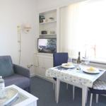 Wohn- und Essbereich mit Sofa, Tisch und TV. Fenster mit Vorhängen.