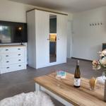 Wohnbereich mit TV, Schrank und Tisch mit Wein und Blumen.