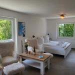 Schlafzimmer mit Bett, Sessel und Tisch. Fenster mit Blick auf Grün.