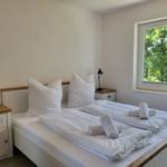 Schlafzimmer mit Doppelbett, zwei Nachttischen und Blick auf grüne Bäume.