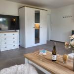 Wohnbereich mit TV, Schrank und Tisch mit Wein und Blumen.