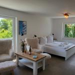 Ein Schlafzimmer mit Bett, zwei Stühlen und Tisch. Durch Fenster blickt man auf Grün.