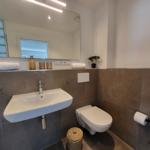 Badezimmer mit Waschbecken, Toilette und Spiegel. Wandfliesen und Handtuch.
